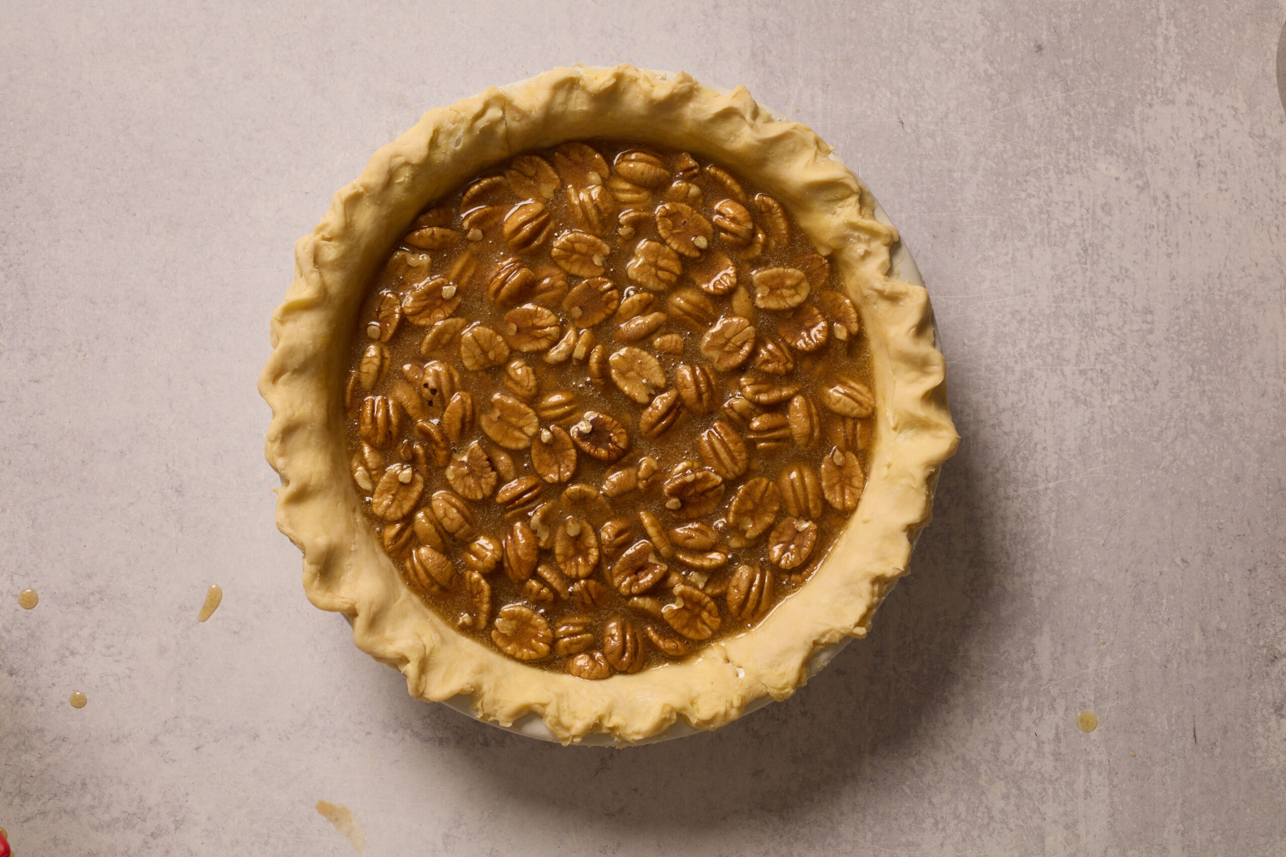 Unbaked pecan pie with a wavy crust, topped with neat pecans, sitting on a light counter.