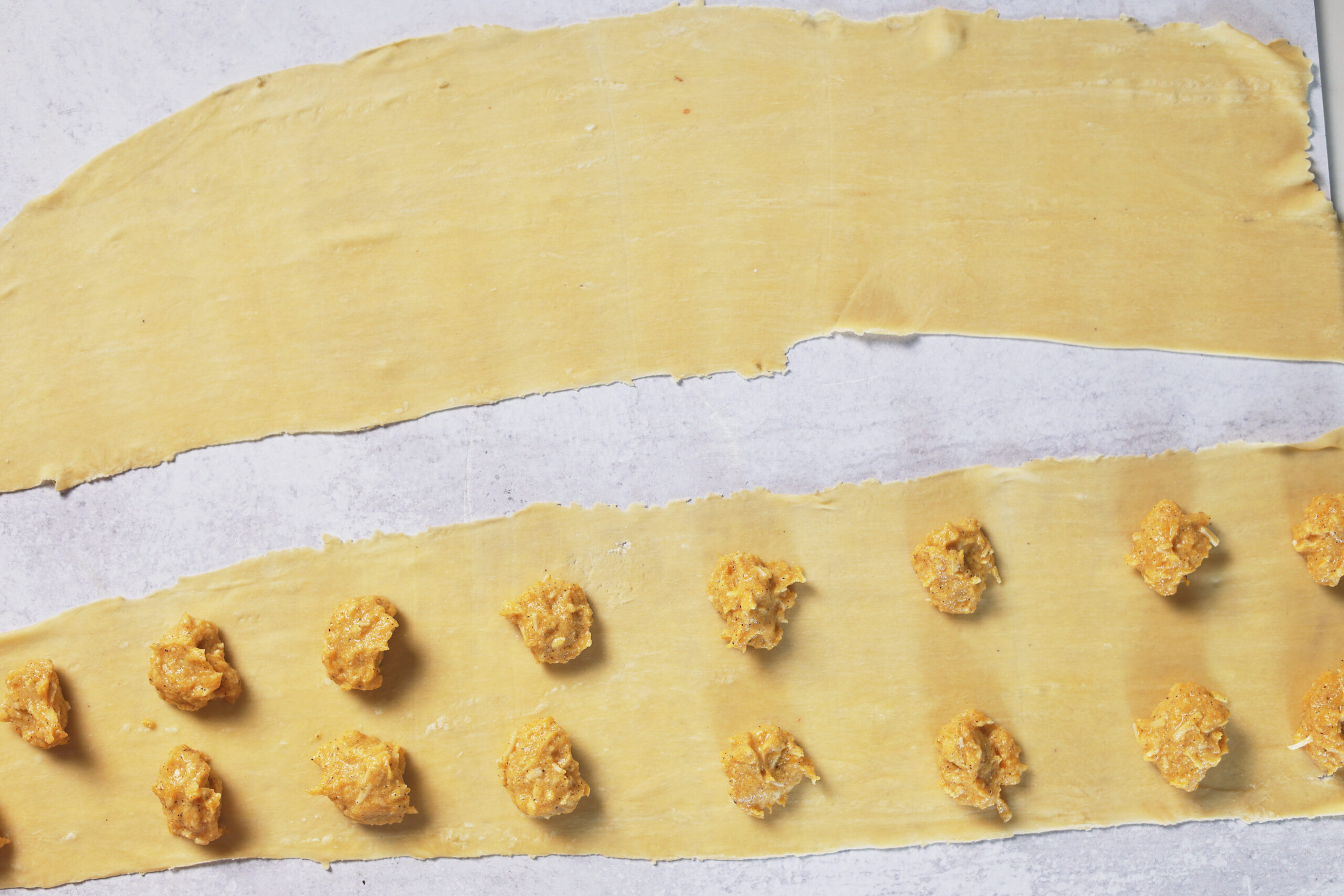 Two pasta dough strips on a table, one topped with little piles of filling&mdash;ready to make some tasty filled pasta!.