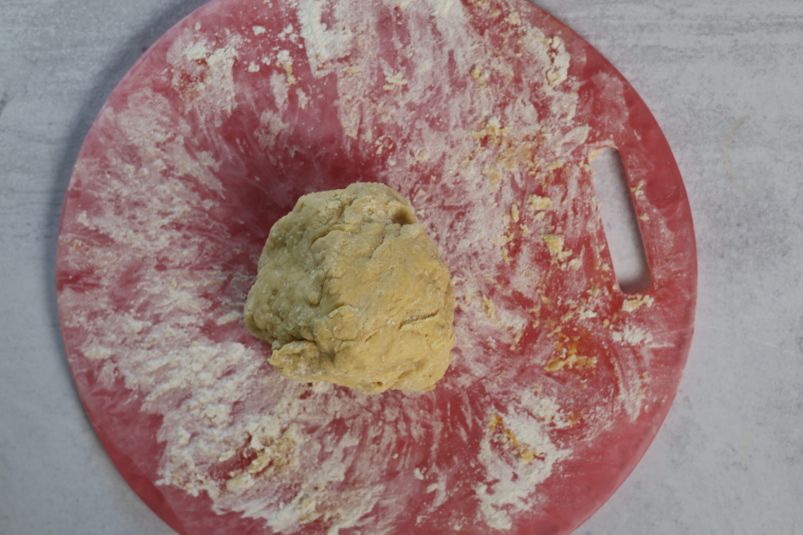 A dough ball chills on a floured red cutting board with a handle, just waiting to become butternut squash ravioli.