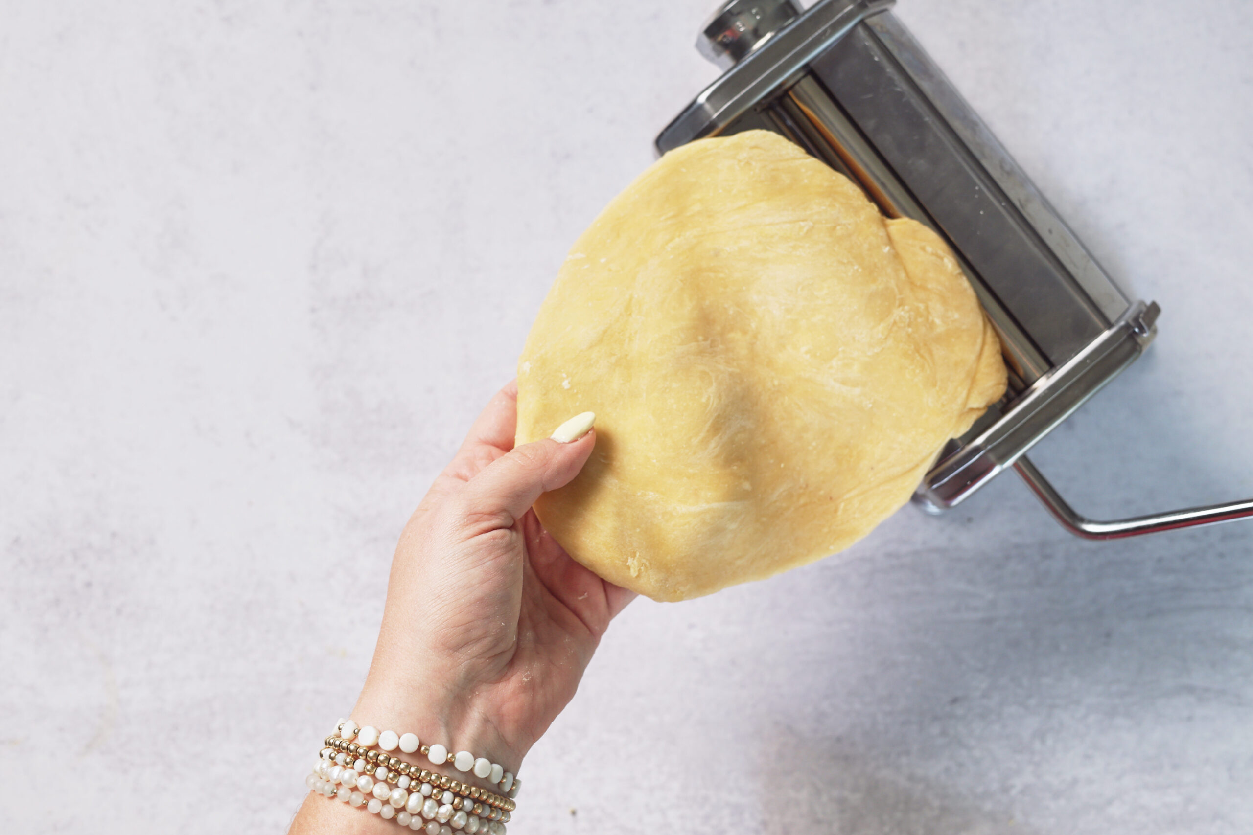 Someone&rsquo;s feeding a sheet of dough into a pasta machine on a pale counter&mdash;time to whip up some fresh, homemade ravioli!.