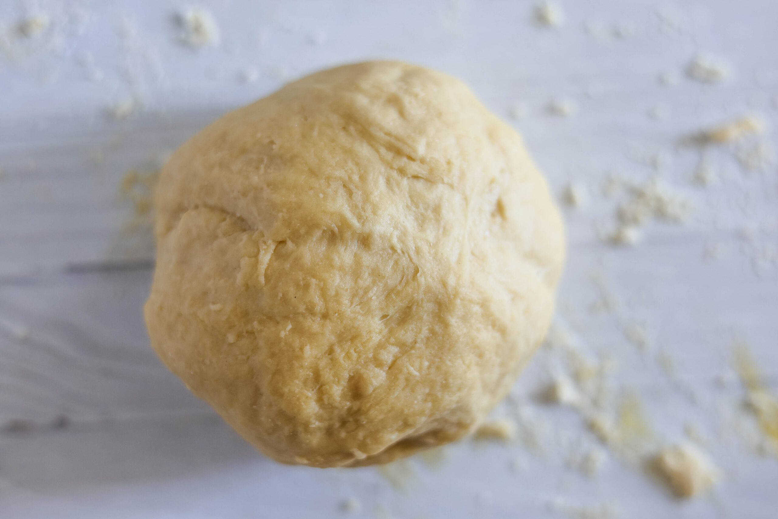 A lump of raw dough chills on a floured white table, ready to become pumpkin ravioli, flour dusted all around.