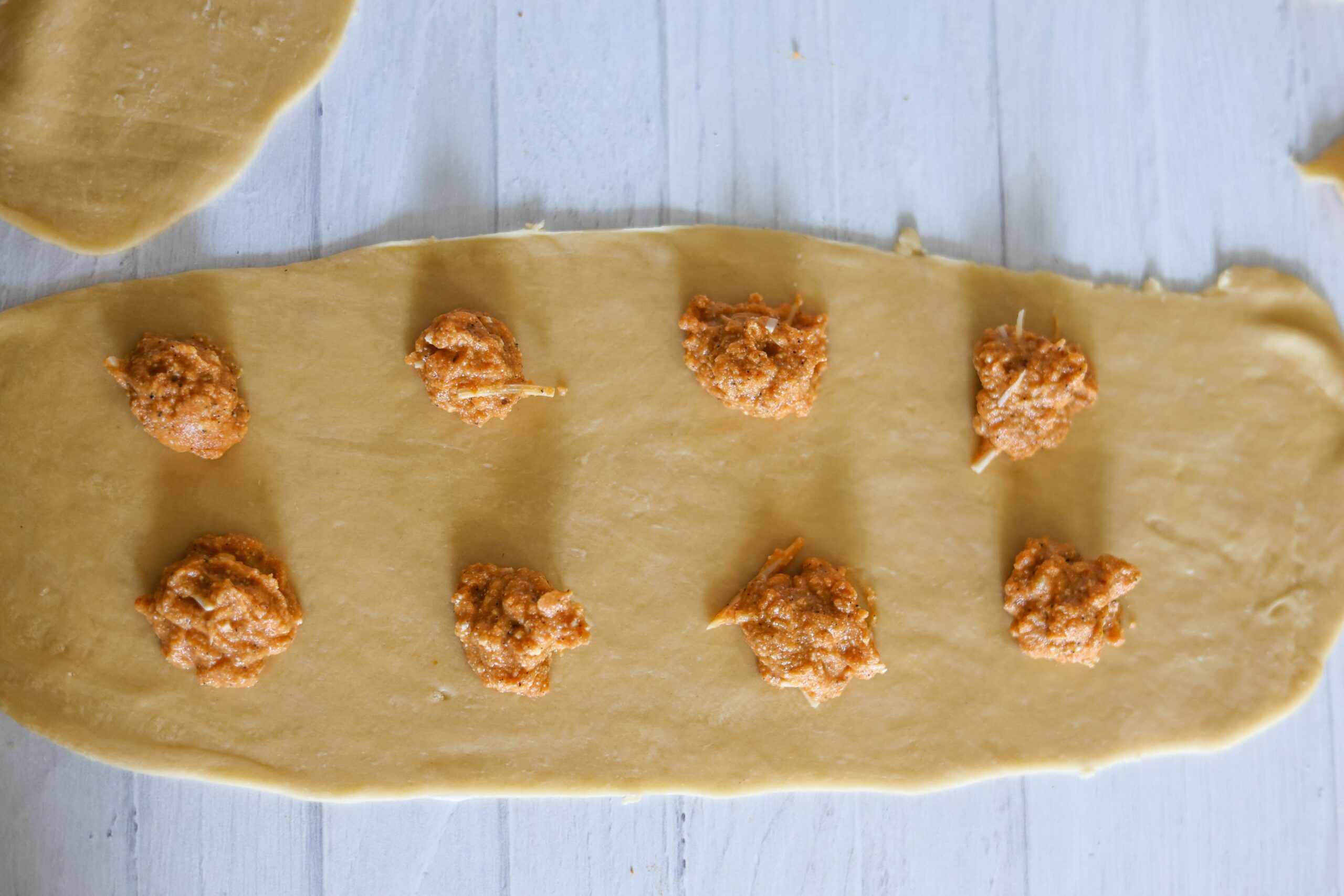 Rolled-out dough on a light counter, with little scoops of pumpkin ravioli filling lined up down the middle.