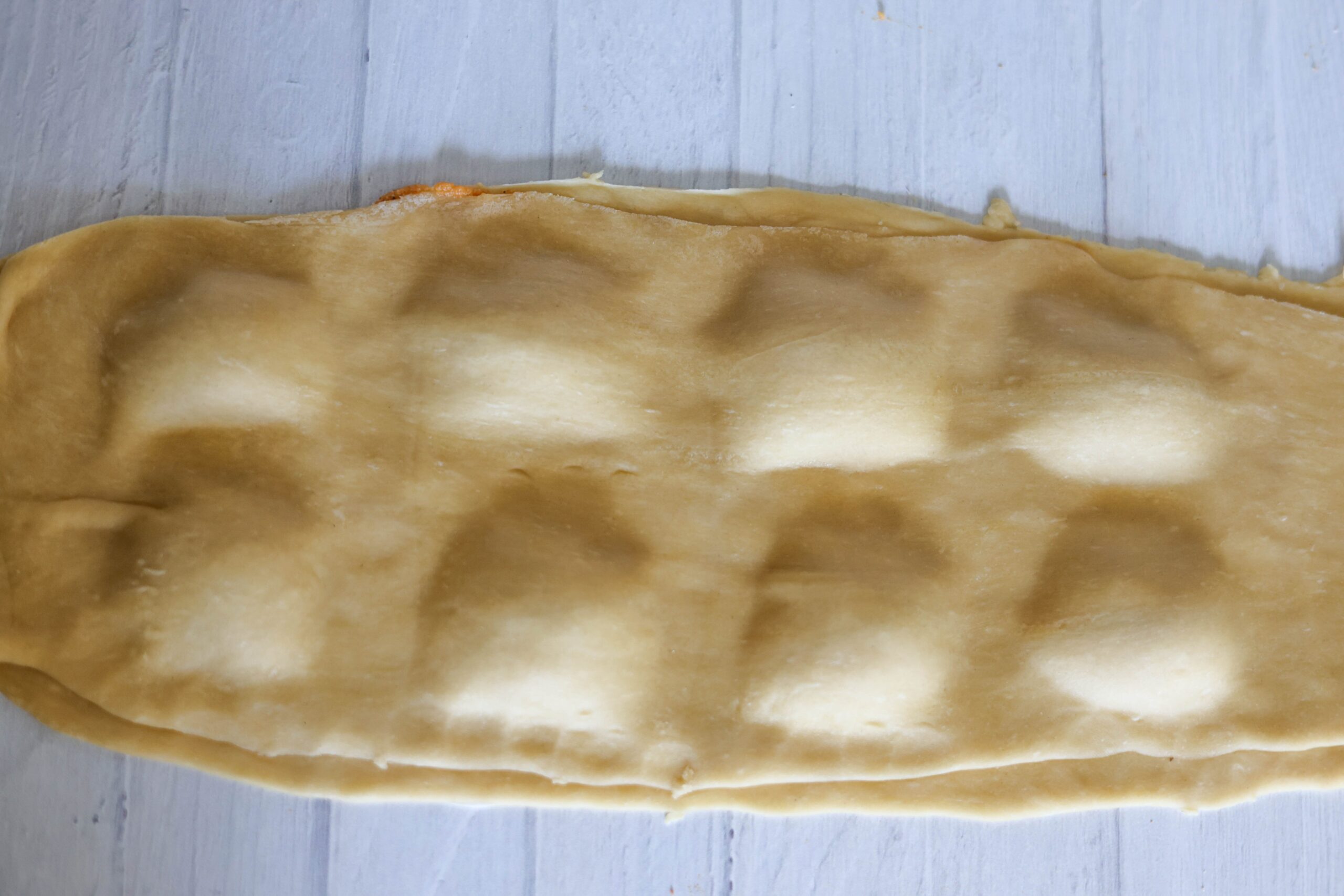 Pasta dough rests over neat pumpkin filling piles, all set to be sliced into ravioli on a light wooden countertop.