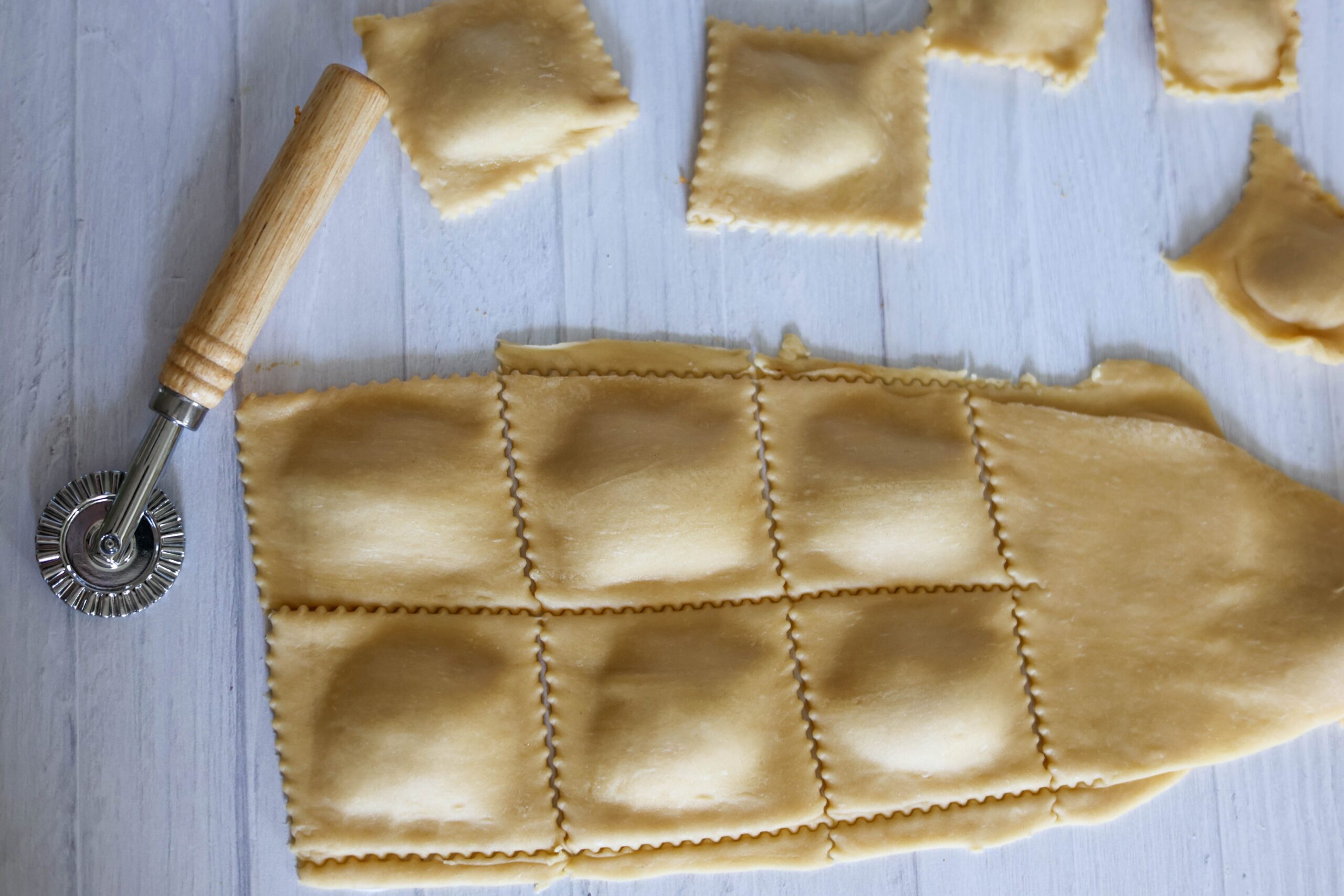 Someone&rsquo;s cutting homemade pumpkin ravioli dough into squares with a wavy pastry wheel, and some ravioli are already finished nearby.
