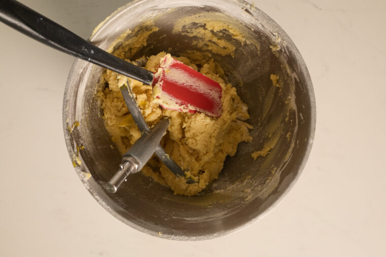 A metal bowl filled with samoa sugar cookie dough, plus a red spatula and paddle beater, chilling on a light countertop.