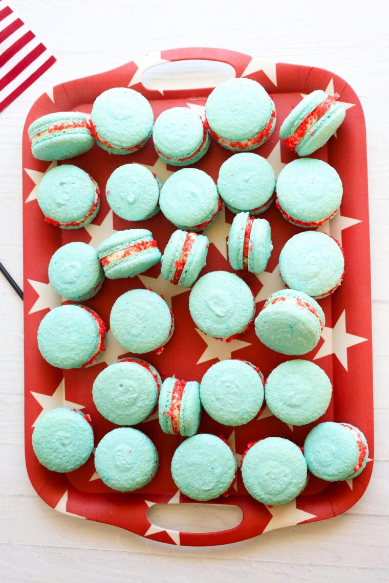 Blue, red, and white rocket pop macarons are lined up on a starry red tray with a US flag showing in the back.