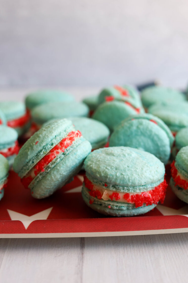 Close-up of rocket pop macarons with blue shells and bright red filling, all lined up on a red tray.