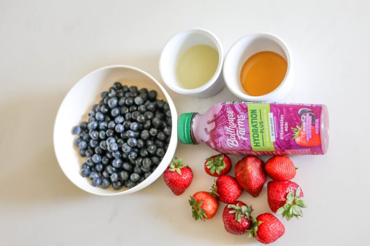 Blueberries, strawberries, a hydration drink, plus two little bowls of liquid on a light surface&mdash;ice pop essentials!.