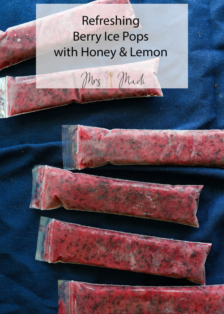 Six homemade berry ice pops in plastic sleeves sit on a dark blue cloth, with &ldquo;Refreshing Berry Ice Pops with Honey & Lemon&rdquo; above.