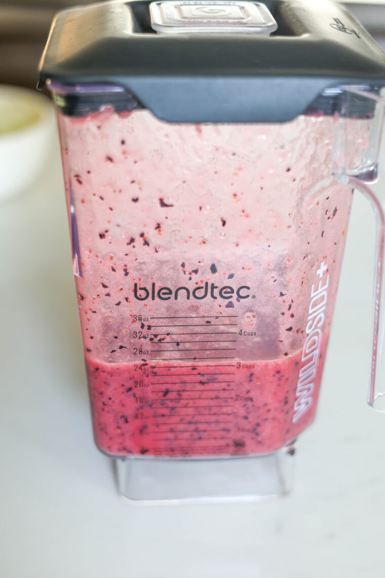 A Blendtec blender jar with a partly-blended red and purple berry mix sits on a white counter, ready for tasty ice pops.