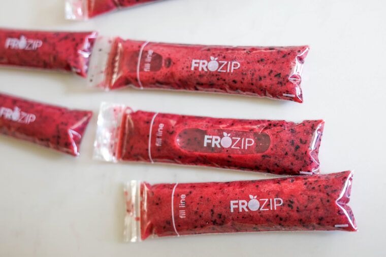 A bunch of FROZIP tubes packed with red, berry-looking frozen mix are chilling on a white background.