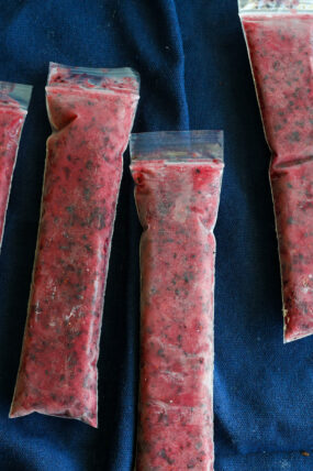 Seven plastic bags stuffed with red, speckled frozen mix&mdash;think berry ice pops&mdash;sit on dark blue fabric.