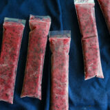 Seven plastic bags stuffed with red, speckled frozen mix&mdash;think berry ice pops&mdash;sit on dark blue fabric.