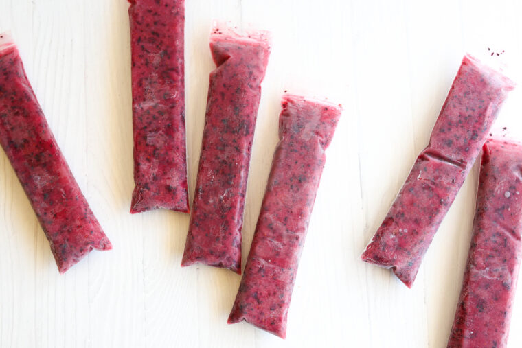 Six bright red berry ice pops in clear sleeves are laid out on a white surface, looking super refreshing and tasty.