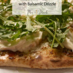 Zoomed-in shot of burrata pizza with creamy sauce, arugula, and balsamic drizzle. Text says: “White Sauce Burrata Pizza.”.