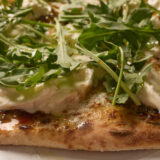A slice of burrata pizza loaded with gooey cheese and fresh arugula sits on a white plate, close-up.
