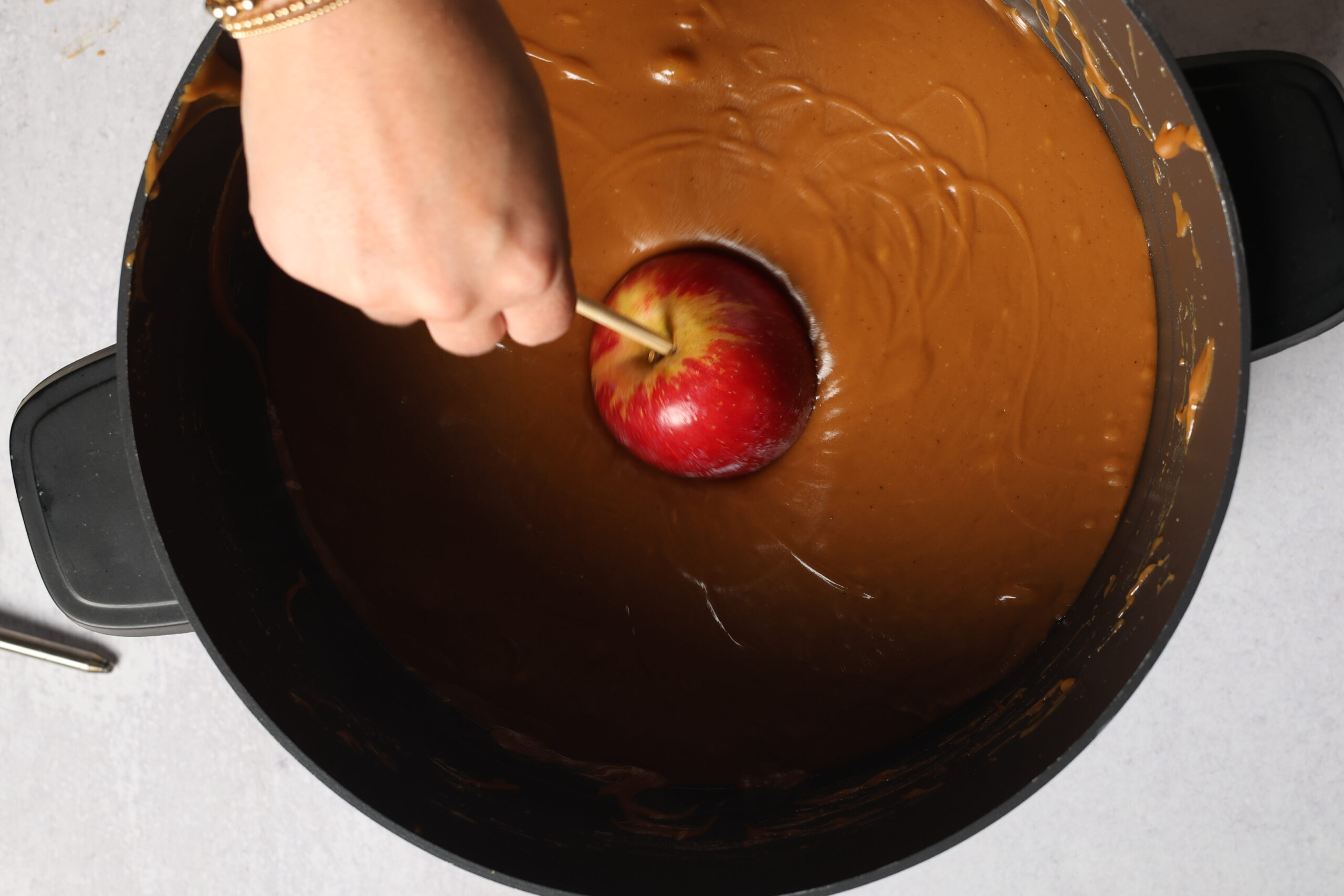 Someone dipping a shiny red apple into gooey melted caramel to make that classic sweet caramel apple treat.