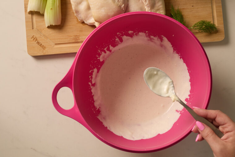 Someone&rsquo;s about to mix up chicken salad&mdash;spoonful of white sauce over a pink bowl, with raw chicken, celery, and grapes nearby.