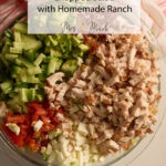 A glass bowl packed with chopped salad—grilled chicken, cucumbers, tomatoes, eggs—tagged as Grilled Chicken Chopped Salad.