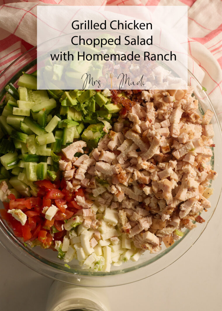 A glass bowl packed with chopped salad&mdash;grilled chicken, cucumbers, tomatoes, eggs&mdash;tagged as Grilled Chicken Chopped Salad.