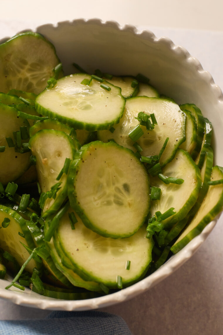 A white bowl filled with thin cucumber slices and chives, lightly seasoned for a crisp, refreshing salad ready in minutes.