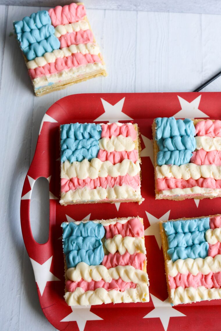 Squares of cake topped with American flag-inspired red, white, and blue frosting on a starry tray&mdash;perfect party treats!.