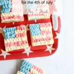 Four flag-themed sugar cookie bars with red, white, and blue frosting sit on a starry red tray next to a flag and spatula.