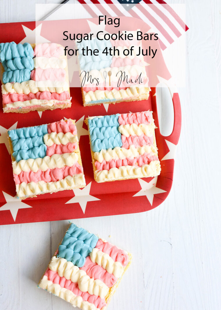 Four flag-themed sugar cookie bars with red, white, and blue frosting sit on a starry red tray next to a flag and spatula.