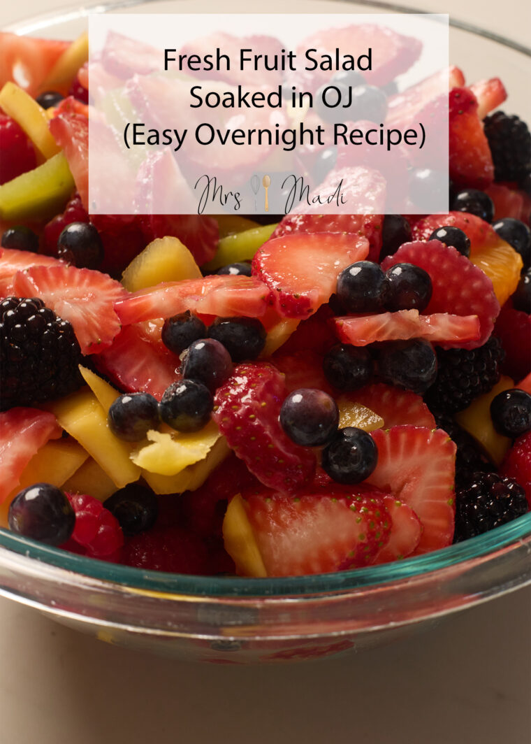 Glass bowl with strawberries, blueberries, blackberries, raspberries & mango in OJ. Text: Fresh Fruit Salad in OJ.
