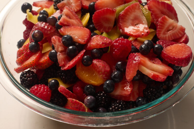 A clear bowl packed with juicy strawberries, blueberries, raspberries, blackberries, and oranges tossed in OJ.