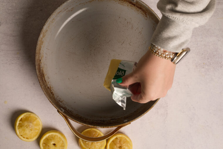 Someone’s about to drop butter into a worn pan, with squeezed lemon halves nearby—looks like homemade lemon ricotta pancakes!.