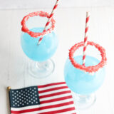 Two blue slushies with red sugar rims and striped straws sit next to a tiny American flag on a white table.
