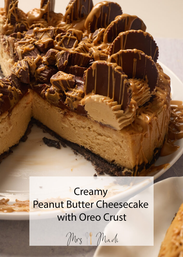 A rich peanut butter cheesecake with an Oreo crust, loaded with PB cups and drizzle, sits on a plate missing a slice.