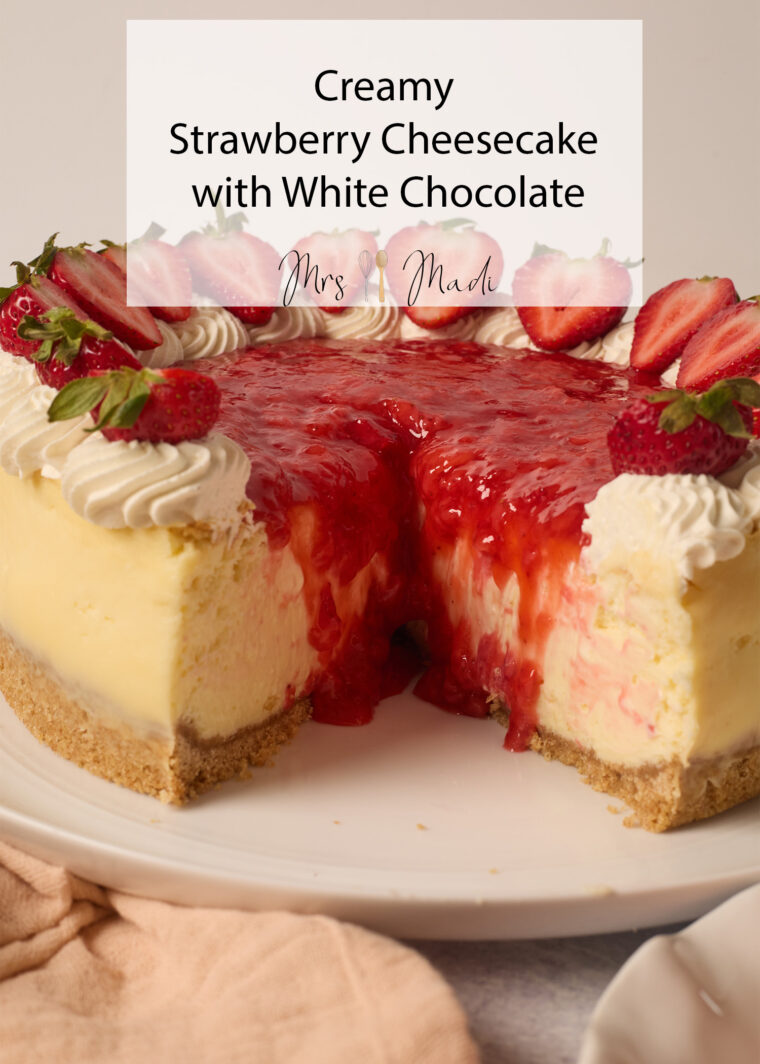 A slice of creamy strawberry cheesecake loaded with sauce, white chocolate, whipped cream, and fresh strawberries on a plate.
