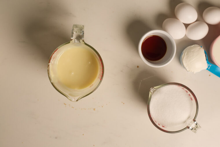 Baking goodies on the counter: condensed milk, sugar, vanilla, eggs, and sour cream&mdash;ready for a creamy strawberry cheesecake!.