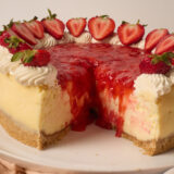 A rich strawberry cheesecake on a graham crust, loaded with sauce, whipped cream, and berry halves&mdash;missing one tasty slice.