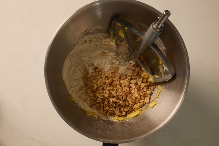 A stand mixer&rsquo;s paddle stirs flour, oats, and chopped peanuts for Crispy Shortbread Tagalongs on a marble counter.