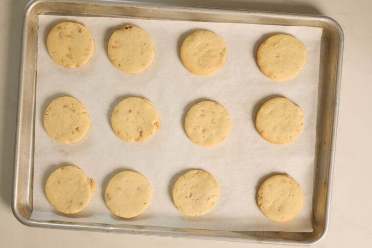 A tray with parchment paper has twelve golden peanut butter cookies all lined up and looking super tasty.