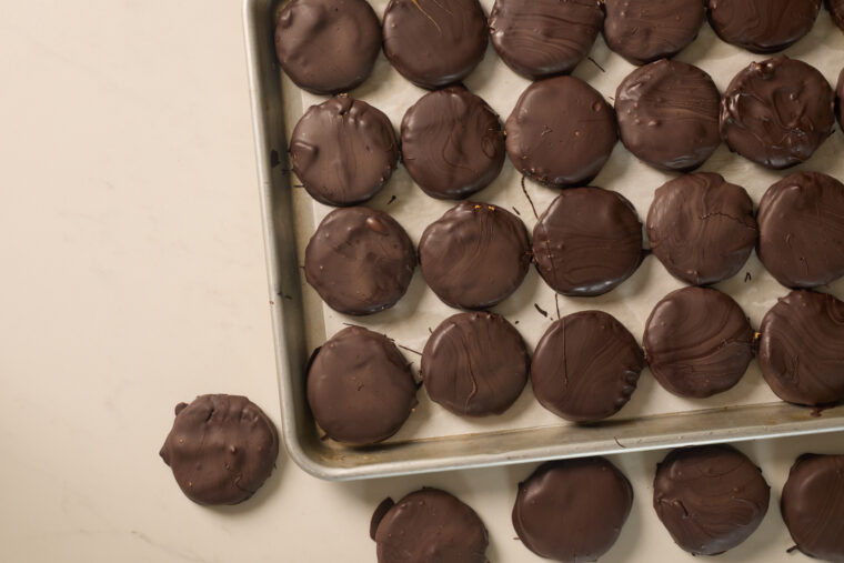 A tray piled with Tagalong-style cookies&mdash;chocolate, peanut butter, shortbread&mdash;sits by a few more on a pale surface.