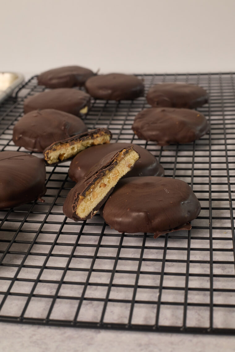 Chocolate-covered cookies, like Tagalongs, sit on a black cooling rack&mdash;one&rsquo;s split to show off the creamy inside.