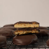 A bunch of Tagalongs-style cookies stacked up, chocolate outside and creamy peanut butter inside, on a black cooling rack.