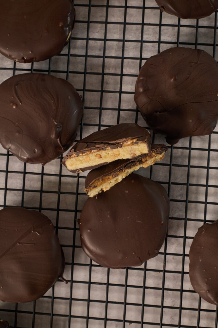 Chocolatey tagalongs chill on a black rack, with one split open to show off its tasty layered filling.
