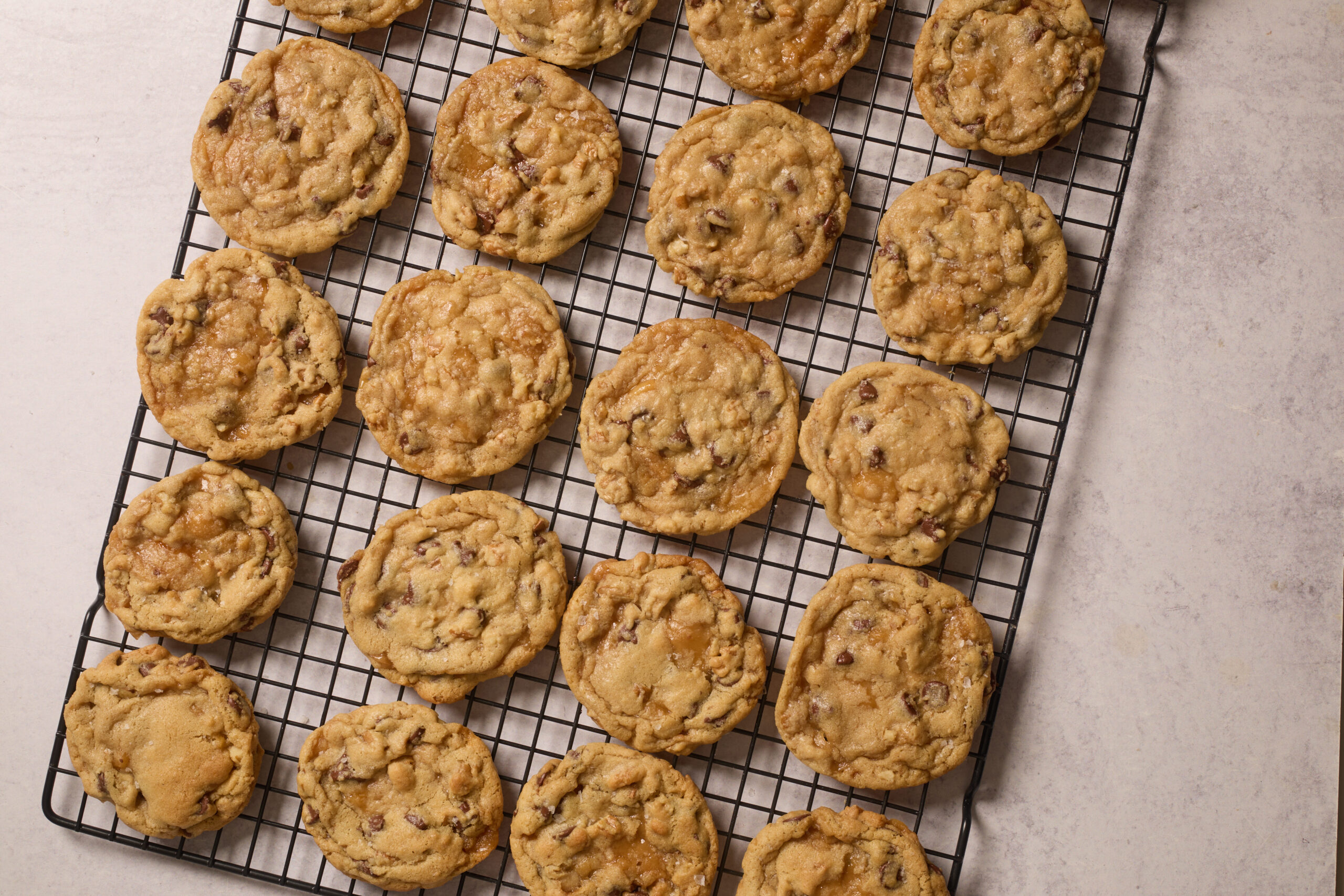 Freshly baked chocolate chip cookies lined up on a cooling rack over a light countertop, ready to eat.
