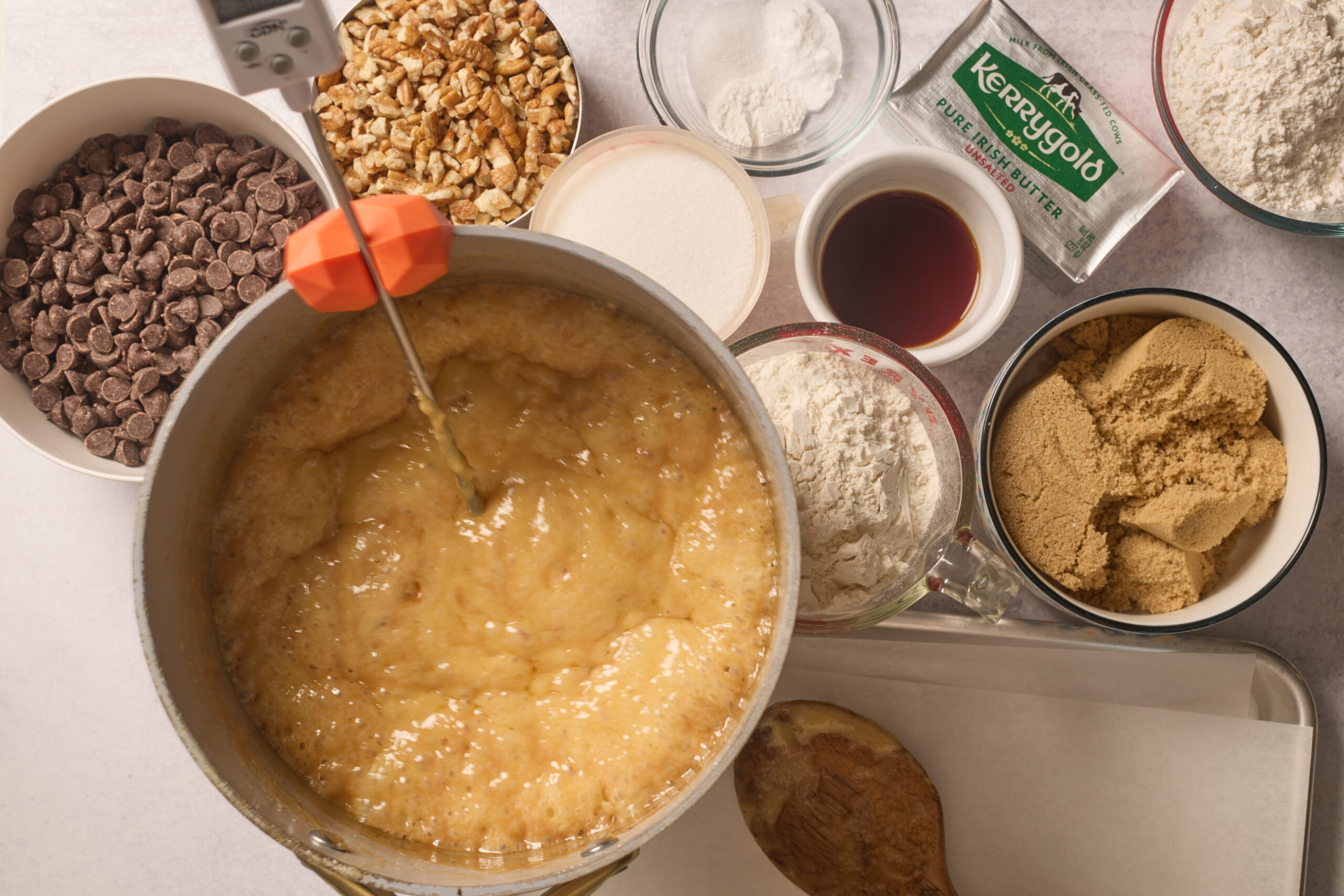 Top-down shot of cookie fixings: bubbling caramel, chocolate chips, walnuts, flour, sugars, vanilla, butter, and pan.