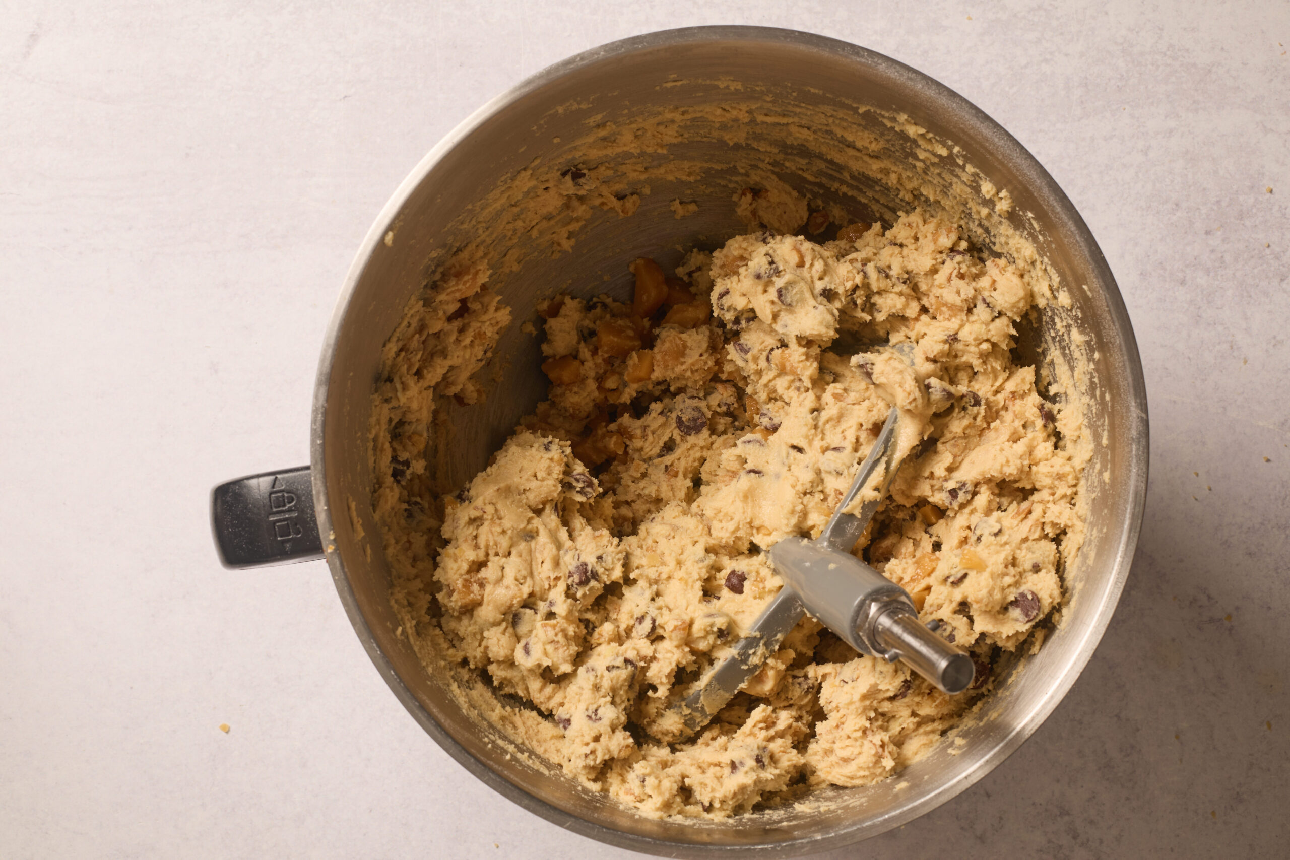 A bowl of pecan cookie dough and chocolate chips sits on a light counter, paddle attachment still in place.