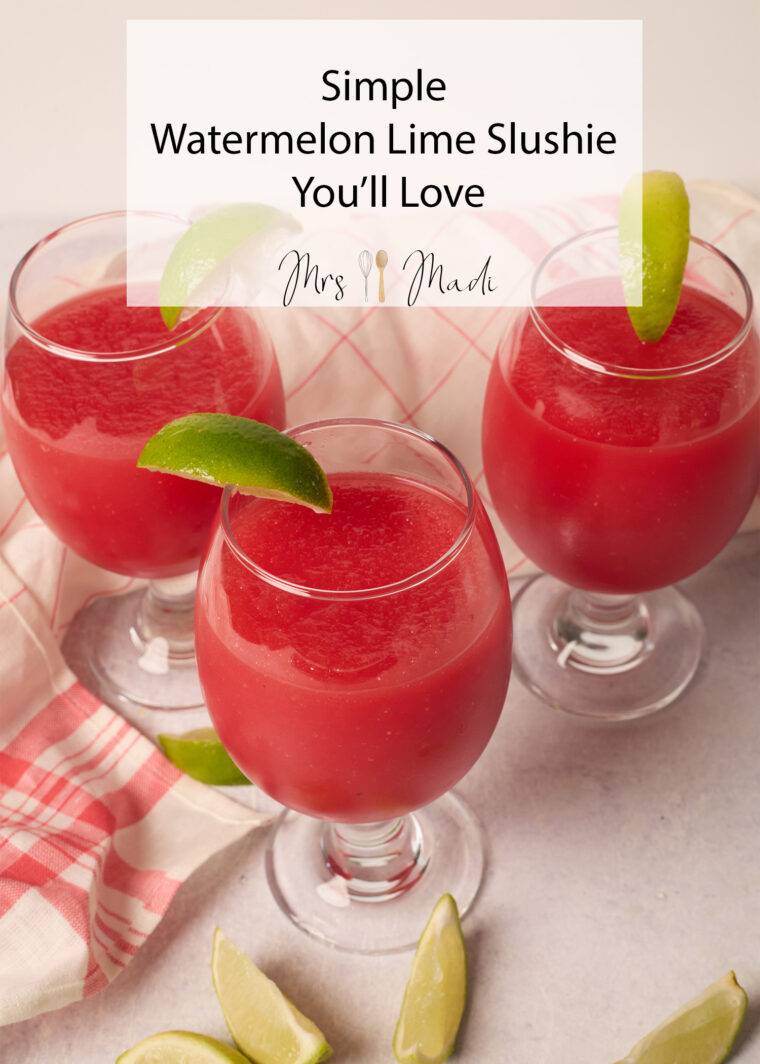 Three glasses of bright watermelon-lime slushie with lime wedges sit on a light table with sliced limes and a pink checkered cloth.