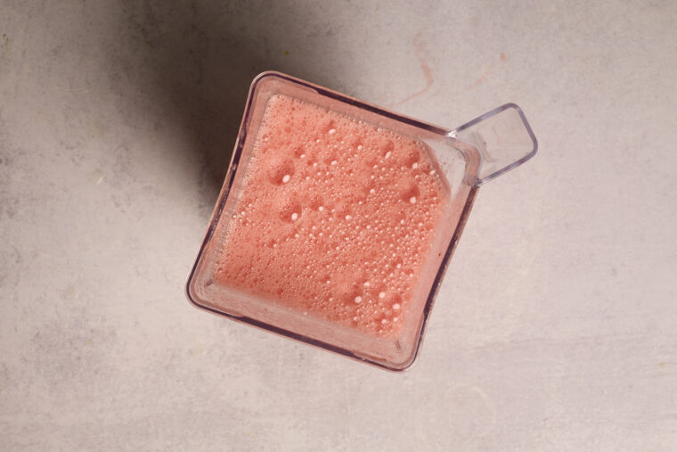 Looking down at a blender packed with pink, frothy watermelon slush, ready to pour&mdash;lime vibes included.