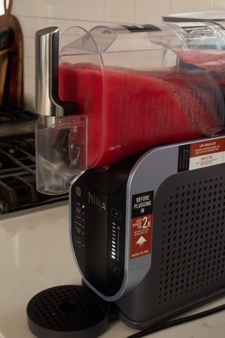 A Ninja countertop gadget pours bright watermelon slushi into a cup, with a &ldquo;before plugging in&rdquo; label on display.
