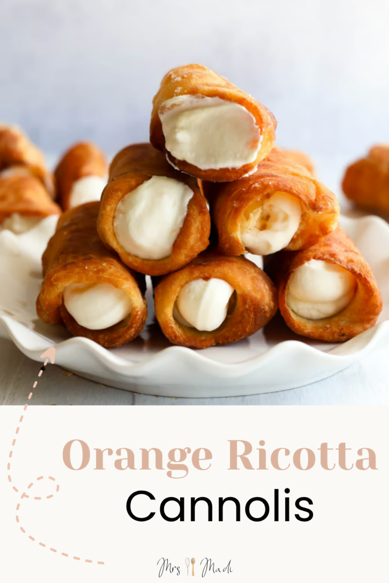 A pile of cannoli stuffed with orange ricotta cream is stacked on a white plate, and you can see even more tasty cannoli hanging out in the background.