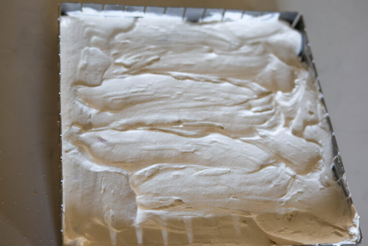 A metal baking pan with a thick layer of white whipped cream or frosting spread smoothly on top—this is just waiting to be turned into some tasty No-Bake Strawberry Shortcake Icebox Bars.